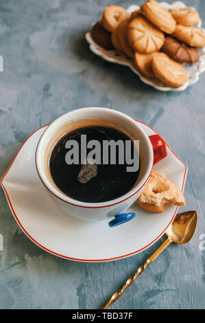 Chocolat chaud le matin dans la tasse blanche originale avec un bouton bleu sur le fond de biscuits. Le petit-déjeuner revigorant. Banque D'Images