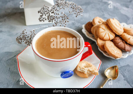 Chocolat chaud le matin dans la tasse blanche originale avec un bouton bleu sur le fond de biscuits. Le petit-déjeuner revigorant. Banque D'Images