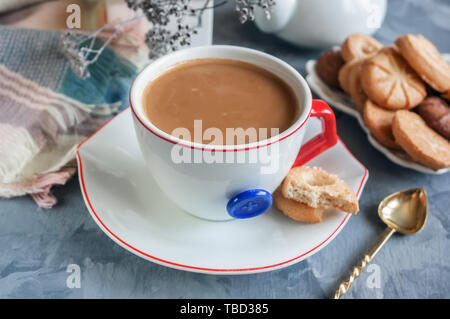 Chocolat chaud le matin dans la tasse blanche originale avec un bouton bleu sur le fond de biscuits. Le petit-déjeuner revigorant. Banque D'Images