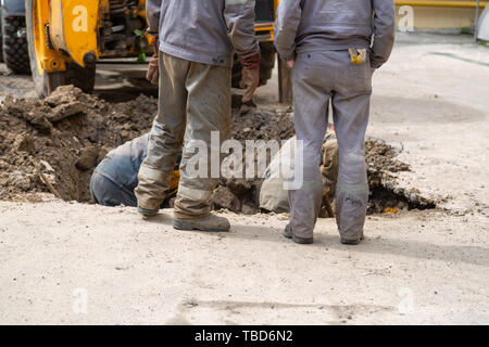 Plusieurs travailleurs en salopette, creuser un trou pour le dépannage de la plomberie. Banque D'Images
