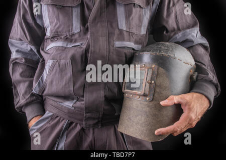 Un employé de la production de vêtements de travail avec un masque de soudage à main. Vêtements de travail spéciaux pour les employés. Fond sombre. Banque D'Images