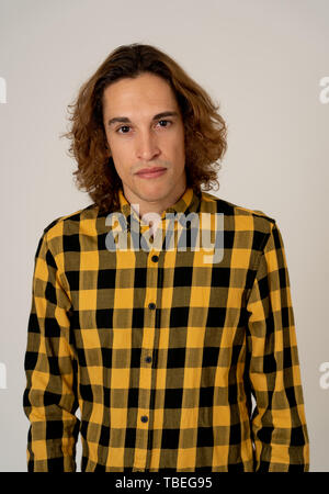 Studio portrait de jeune adolescent homme avec de longs cheveux bruns portant chemise à carreaux très confiant et détendu à poser et la modélisation. Isolé sur neutra Banque D'Images