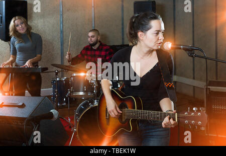 Groupe de jeunes musiciens passionnés avec la chanteuse et guitariste émotionnelle qui exercent dans l'enregistrement studio de musique Banque D'Images