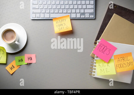 Clavier de l'ordinateur avec une tasse de café et des notes autocollantes sur fond gris. Poisson d'avril farce Banque D'Images