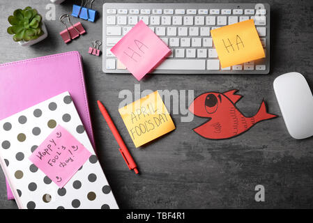 Clavier de l'ordinateur avec la papeterie, poisson de papier et des notes autocollantes sur fond gris. Poisson d'avril farce Banque D'Images