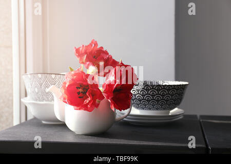 Théière avec de belles fleurs et de la vaisselle sur la table près de window Banque D'Images