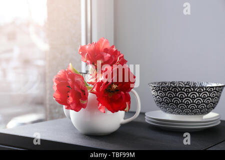 Théière avec de belles fleurs et de la vaisselle sur la table près de window Banque D'Images