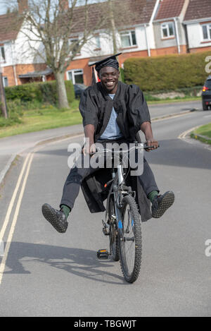 Andover, Hampshire, England, UK. Mai 2019. Un étudiant à l'université wearing cap and gown la bicyclette. Banque D'Images