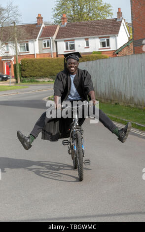 Andover, Hampshire, England, UK. Mai 2019. Un étudiant à l'université wearing cap and gown la bicyclette. Banque D'Images