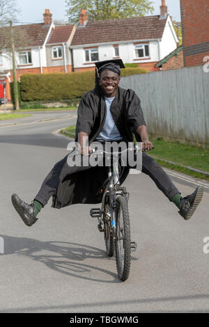 Andover, Hampshire, England, UK. Mai 2019. Un étudiant à l'université wearing cap and gown la bicyclette. Banque D'Images