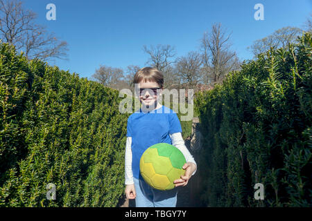 Cinq ans posant avec balle en labyrinthe Bush au parc Slottsskogen, Göteborg, Suède. Banque D'Images