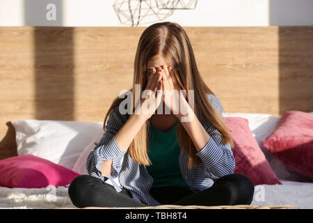 Triste teenage girl sitting on bed at home Banque D'Images