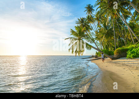 Femme avec chapeau asiatique traditionnel de détente sur la plage tropicale sous sur la noix de coco palmier en rétro-éclairage sunset sunburst de vraies personnes. L'Indonésie, Banyak Isl Banque D'Images