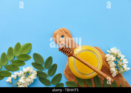 Le miel en pot de verre et d'acacia fleurs sur fond bleu, vue d'en haut Banque D'Images