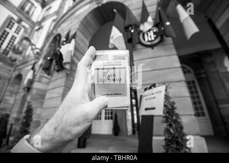 Strasbourg, France - 26 mai 2019 : image de l'homme main tenant l'électeur français voiture Carte Electorale avec l'entrée de l'Hôtel de Ville Hôtel de Ville bureau de vote sur le jour de l'élection du Parlement européen 2019 - noir et blanc Banque D'Images