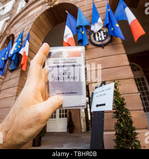 Strasbourg, France - 26 mai 2019 : image de l'homme main tenant l'électeur français voiture Carte Electorale avec l'entrée de l'Hôtel de Ville Hôtel de Ville bureau de vote sur le jour de l'élection du Parlement européen 2019 Banque D'Images