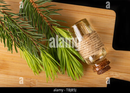 Les jeunes pousses d'épinette et de l'huile dans un plat en verre. Préparations écologique sur une planche de bois. Fond sombre. Banque D'Images