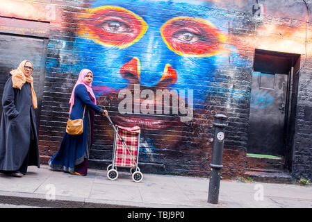 Brick Lane, Shoreditch, London, England, UK - Avril 2019 : deux femmes portant un hijab walking in Brick Lane à côté d'un mur recouvert de graffitis mur Banque D'Images