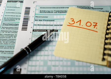 Formulaire de déclaration d'impôt allemand avec un stylo noir en premier plan et un papier jaune indiquant la date limite du 31 juillet prochain. Banque D'Images