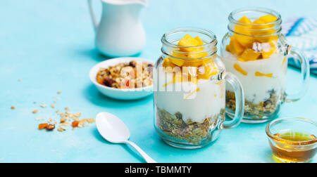 Un petit-déjeuner sain, dessert. Les mangues fraîches avec du yogourt et granola en pots. Arrière-plan de la pierre bleue Banque D'Images