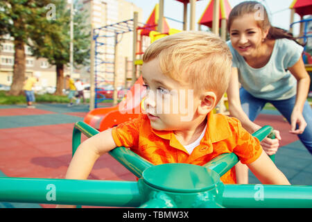 Petit garçon active sur l'aire de jeux. jouer enfant avec mère sur merry go round Banque D'Images