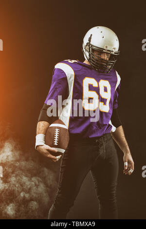Portrait close-up, joueur de football américain, barbu sans casque avec le ballon dans ses mains. Concept de football américain, patriotisme, close-up. Banque D'Images