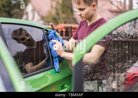 Le nettoyage de printemps. Jeune garçon est la voiture verte de polissage. Banque D'Images