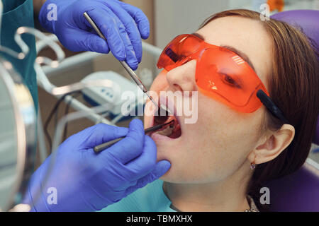 Dentiste examine les dents du patient avec cavité noire à l'aide d'outils de dentiste et de miroir. La carie dentaire dans la bouche d'ouverture libre. Banque D'Images