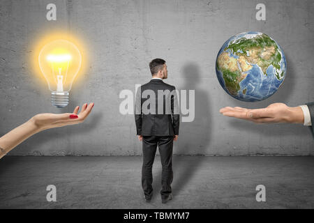 Vue arrière de businessman standing entre deux grandes mains, woman's hand ampoule en lévitation, la main de l'homme peu de terre en lévitation. Banque D'Images