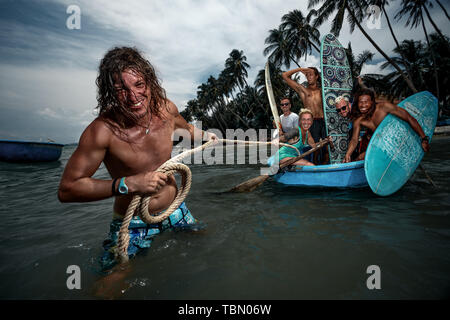 Groupe de surfeurs à bord d'un bateau en bois vietnamien pour surfer session sur le village côtier et un ami transporte le bateau avec des amis Banque D'Images