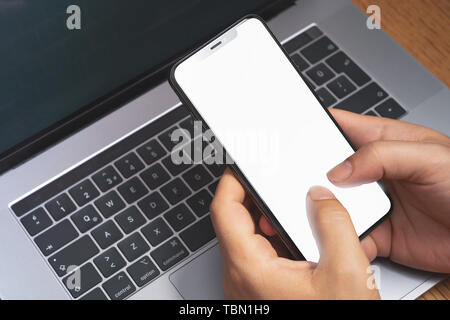 Man holding smartphone via l'ordinateur portable avec écran vide.concept publicitaire de la technologie. Banque D'Images