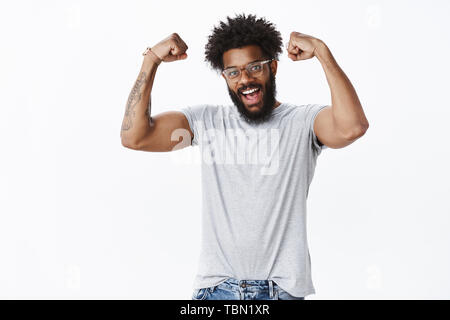 Strong et masculin beau happy african american male à beard dans les verres montrant que l'amélioration de biceps en mains et encourager l'appui de la victoire te Banque D'Images