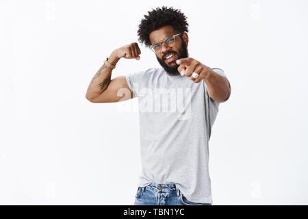 Studio shot of certain auto-satisfait african american sportsman dans les verres avec barbe et cheveux boucles pointant à l'appareil photo avec dédain fronçant showi Banque D'Images