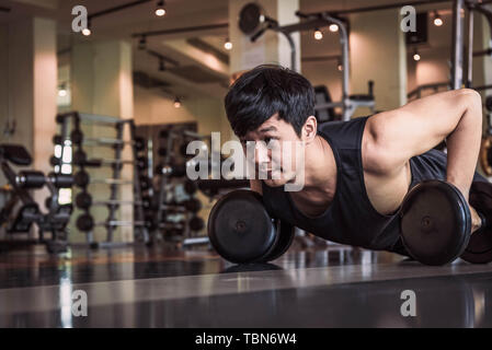 Portrait of Asian man doing fitness poussant l'exercice avec haltère dans une salle de sport. Les gens de vie et Sport concept. Sportsman holding poids par deux part Banque D'Images