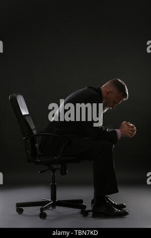 Handsome man sitting on chair contre le fond sombre Banque D'Images