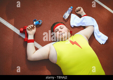 Fat lazy man sleeps fatigué se trouve sur la piste dans le stade. La notion de perte de poids, le régime alimentaire. Vue d'en haut. Banque D'Images