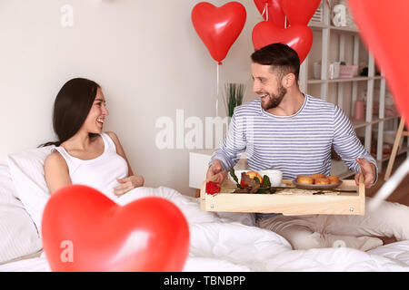 Jeune femme qui reçoit un petit déjeuner au lit de son mari bien-aimé Banque D'Images