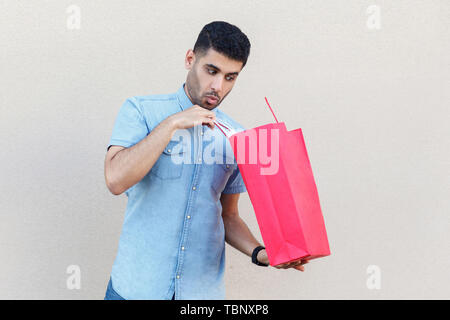 Unboxing et à l'intérieur du sac. Portrait de beau jeune homme barbu en chemise bleu, rouge permanent holding Shopping bag, à l'intérieur. Piscine st Banque D'Images