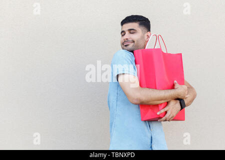 Le meilleur cadeau jamais. Portrait de beau jeune homme barbu en chemise bleue debout, serrant ses jolies sac shopping rouge ou don et d'apprécier. Piscine st Banque D'Images