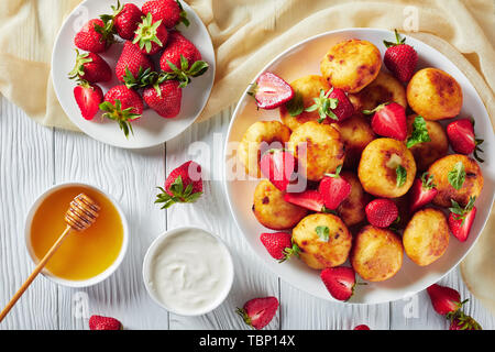Vue de dessus de fromage cottage avec crêpes aux fraises sur une plaque blanche sur une table en bois avec du miel, de la crème sure et de fraises fraîches dans Banque D'Images