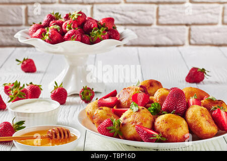 Close-up de fromage cottage donuts servi avec des fraises sur une plaque sur une table en bois avec du miel, de la crème sure et de fraises fraîches dans un bol de fruits Banque D'Images