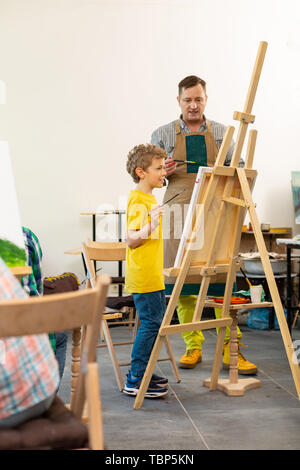 Aider les élèves créatifs. Professeur d'art de porter un tablier à aider son jeune élève près de chevalet de dessin Banque D'Images