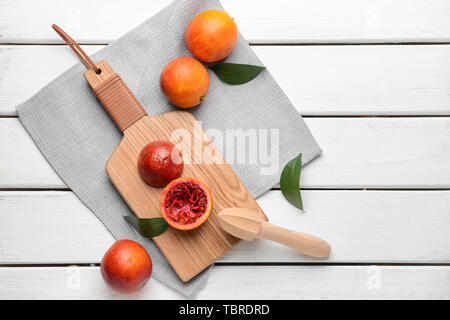 Planche à découper et un presse-agrumes avec du sang frais des oranges sur tableau blanc Banque D'Images