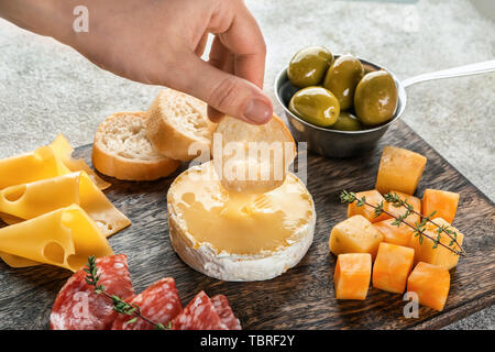 Femme trempant du pain dans le fromage sur planche de bois Banque D'Images