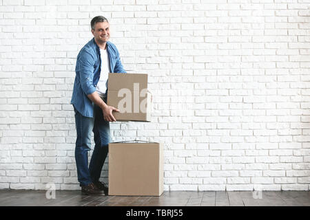 Handsome man avec moving boxes près de white brick wall Banque D'Images