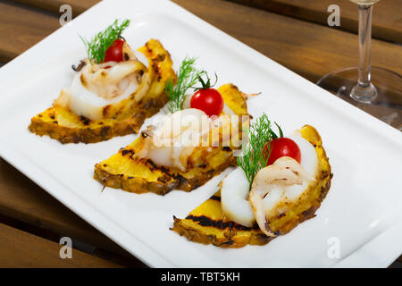 Photographie de la plaque avec sepia frits sur une grille avec de l'ananas, de tomates cerises et de la sauce Chili dans le restaurant. Banque D'Images