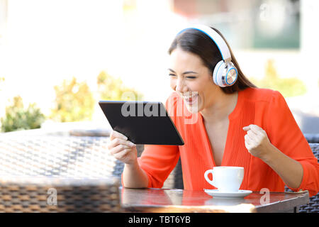 Excited woman regarder et écouter sur media tablet assis dans un café terrasse Banque D'Images