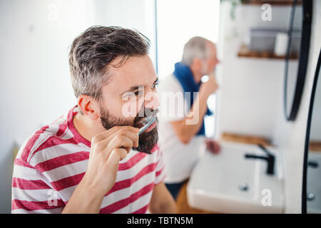 Un adulte hipster fils et père supérieur se brosser les dents à l'intérieur à la maison. Banque D'Images