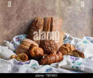 Différents types de bicarbonate de still life. Brioches croissants, muffins et pains, galettes de pain sur le textile avec broderie fleurs de draperie. Style rustique Banque D'Images