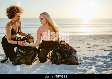 Deux femmes picking up trash de la plage. Les femelles le nettoyage de la plage et de la collecte des déchets dans le sac poubelle. Banque D'Images